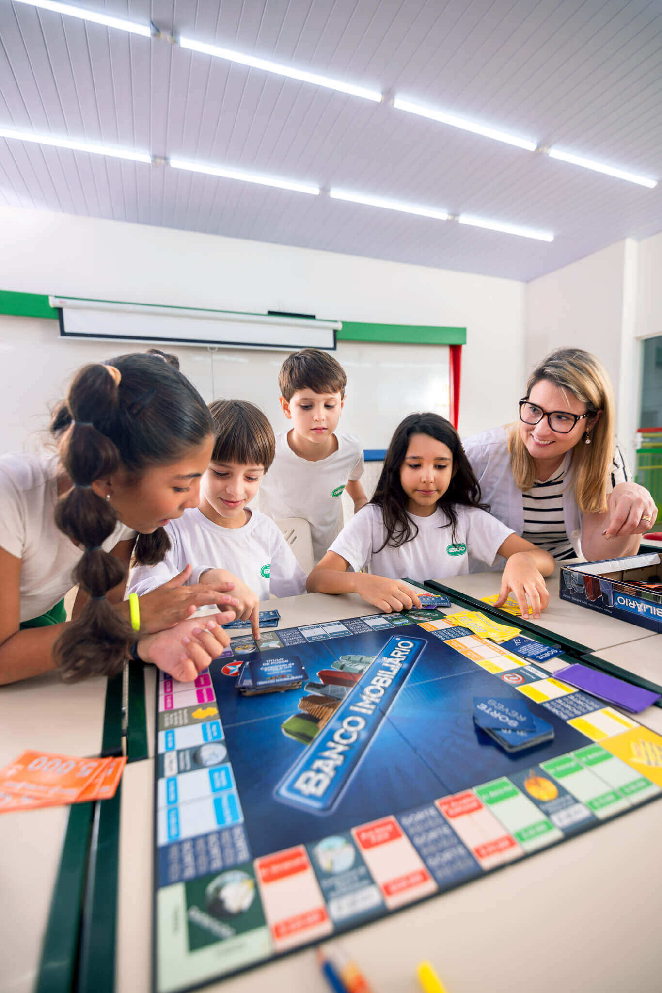 Alunos jogando jogo de tabuleiro sobre finanças com a professora